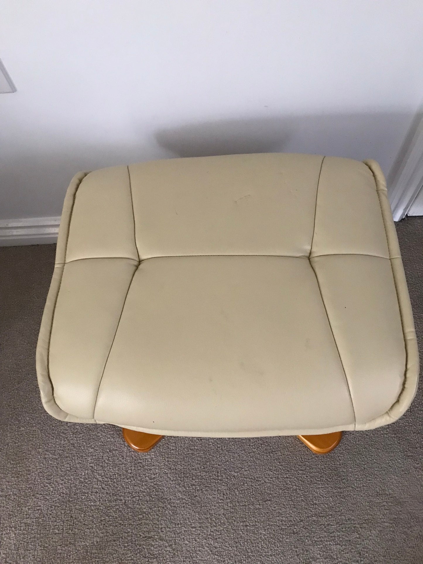 Cream faux leather footstool with wooden legs to match recliner chair.